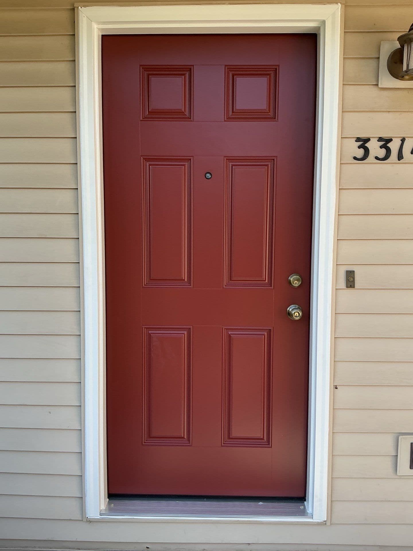 Deep burgundy six-panel front door with white trim, beige siding, brass hardware, and partial house number 331; a neat, welcoming entryway.